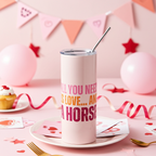 Pink tumbler with 'All you need is love and a horse' text on a pink tablecloth with balloons and party decorations.
