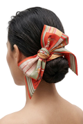 A woman shown from the back wearing a large decorative hair bow made from a patterned silk scarf tied around her low bun.