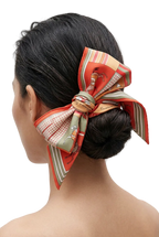 A woman shown from the back wearing a large decorative hair bow made from a patterned silk scarf tied around her low bun.