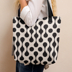 A woman in a white shirt stands in profile holding a canvas tote bag with a black and white wavy dot pattern.