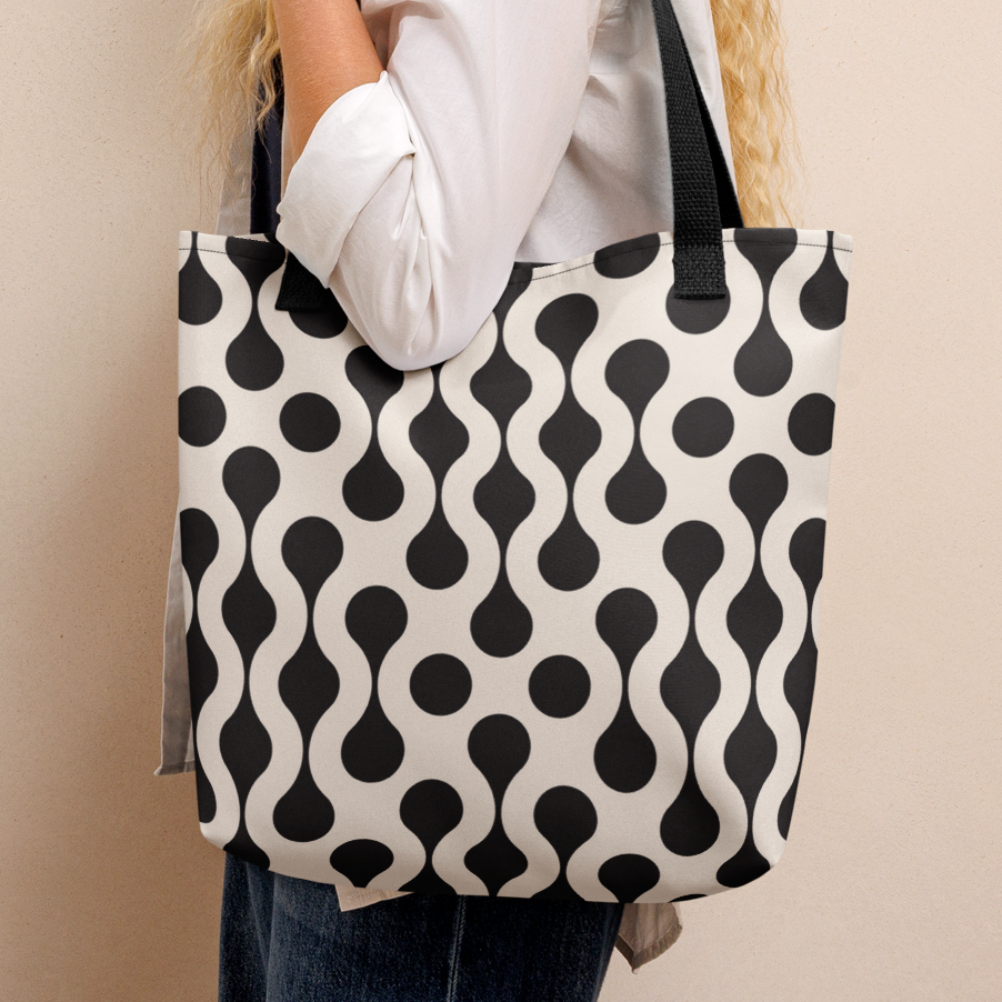 A woman in a white shirt stands in profile holding a canvas tote bag with a black and white wavy dot pattern.