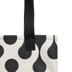 Close-up of a tote bag corner showing a black-and-white teardrop pattern with a black woven handle.