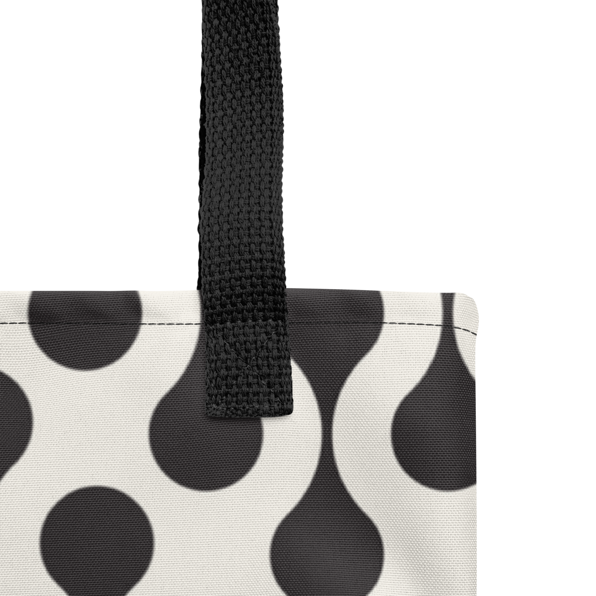 Close-up of a tote bag corner showing a black-and-white teardrop pattern with a black woven handle.