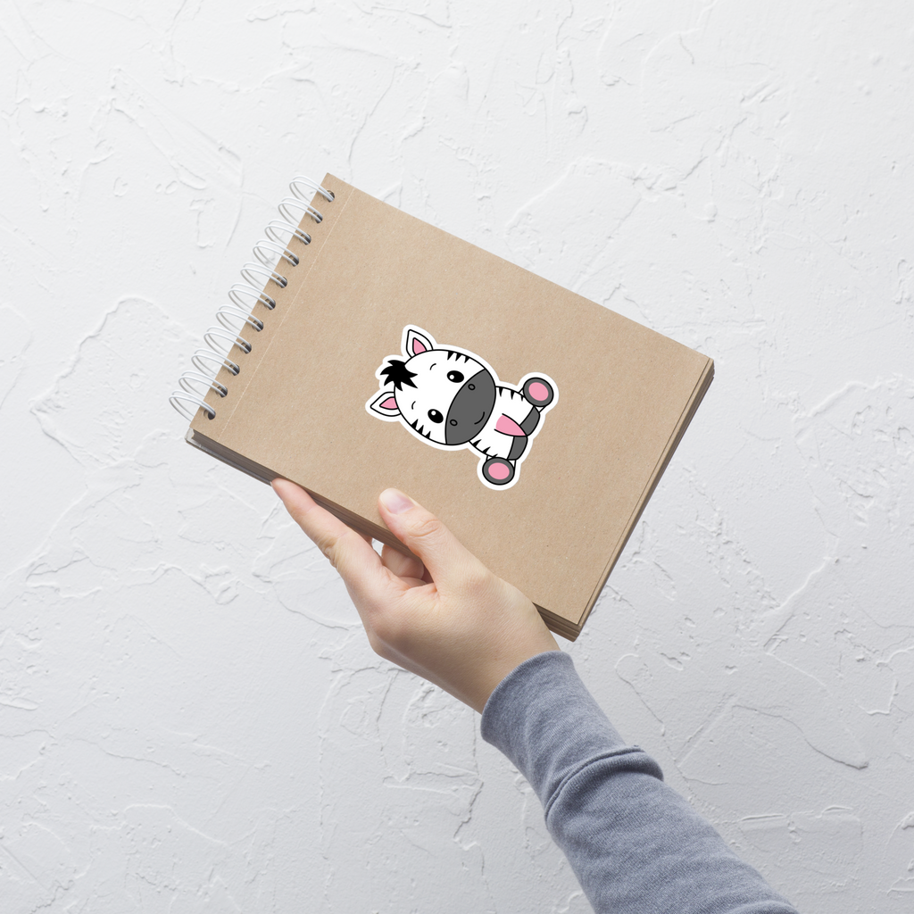 Hand holding a brown notebook with a cartoon pony sticker on a light gray background