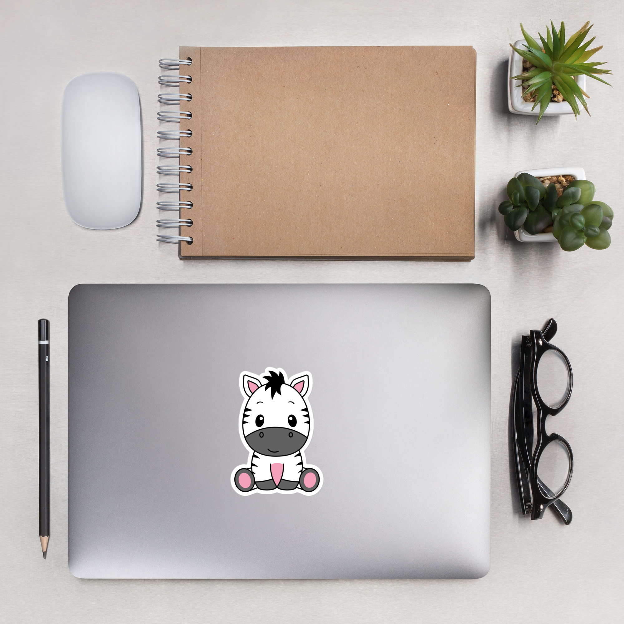 Laptop with a pony sticker on a desk with a notebook, mouse, pencil, and glasses.
