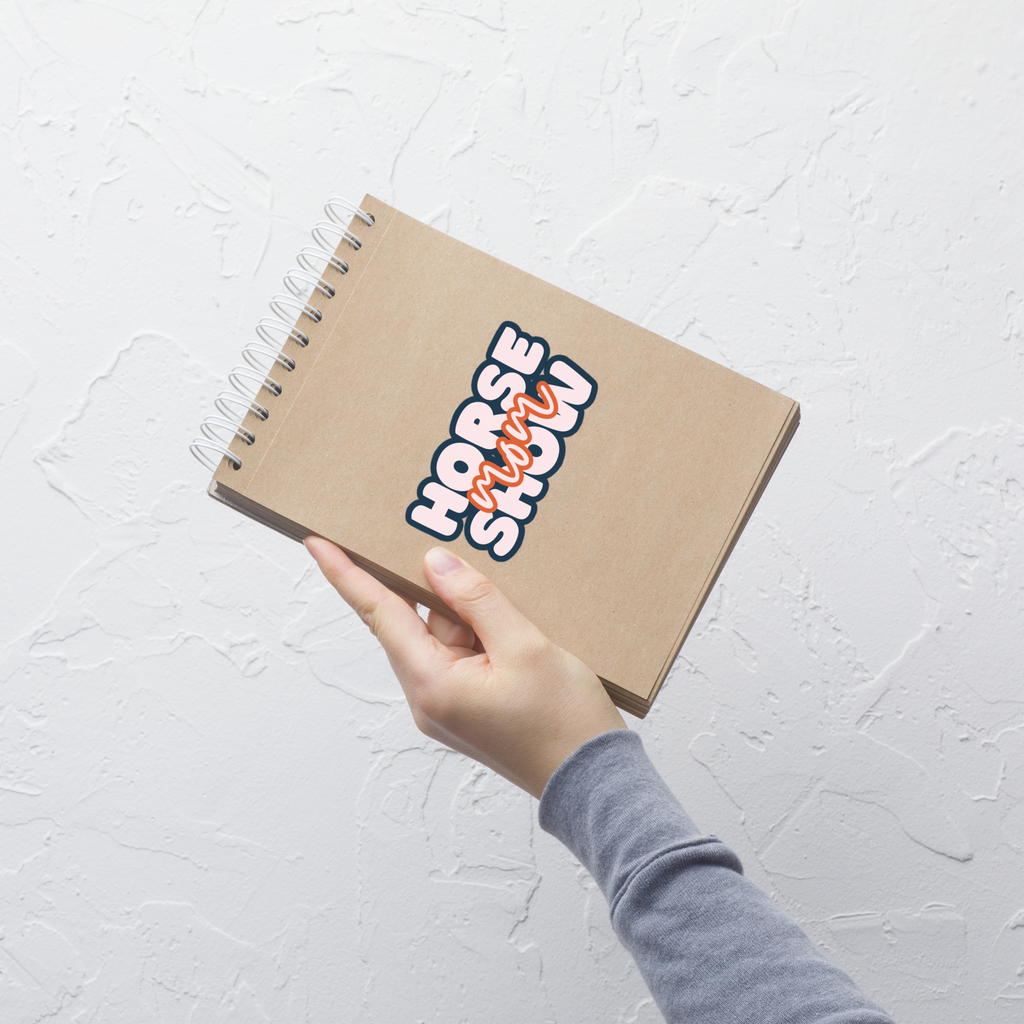 Notebook with 'Horse Show' sticker held by a hand on a light gray background