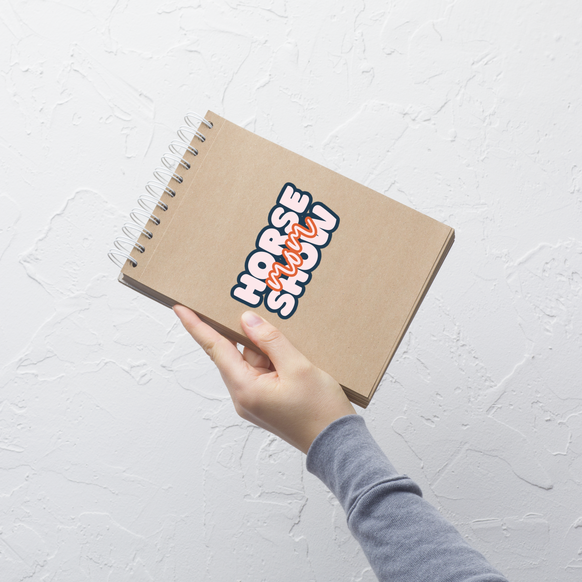 Notebook with 'Horse Show' sticker held by a hand on a light gray background