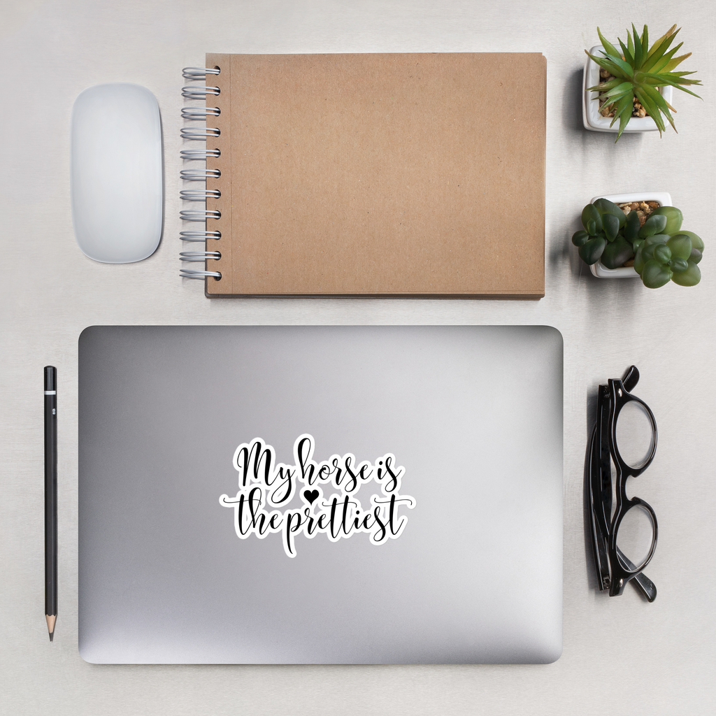 Laptop with 'My horse is the prettiest' sticker, notebook, mouse, pencil, glasses, and plants on a light surface