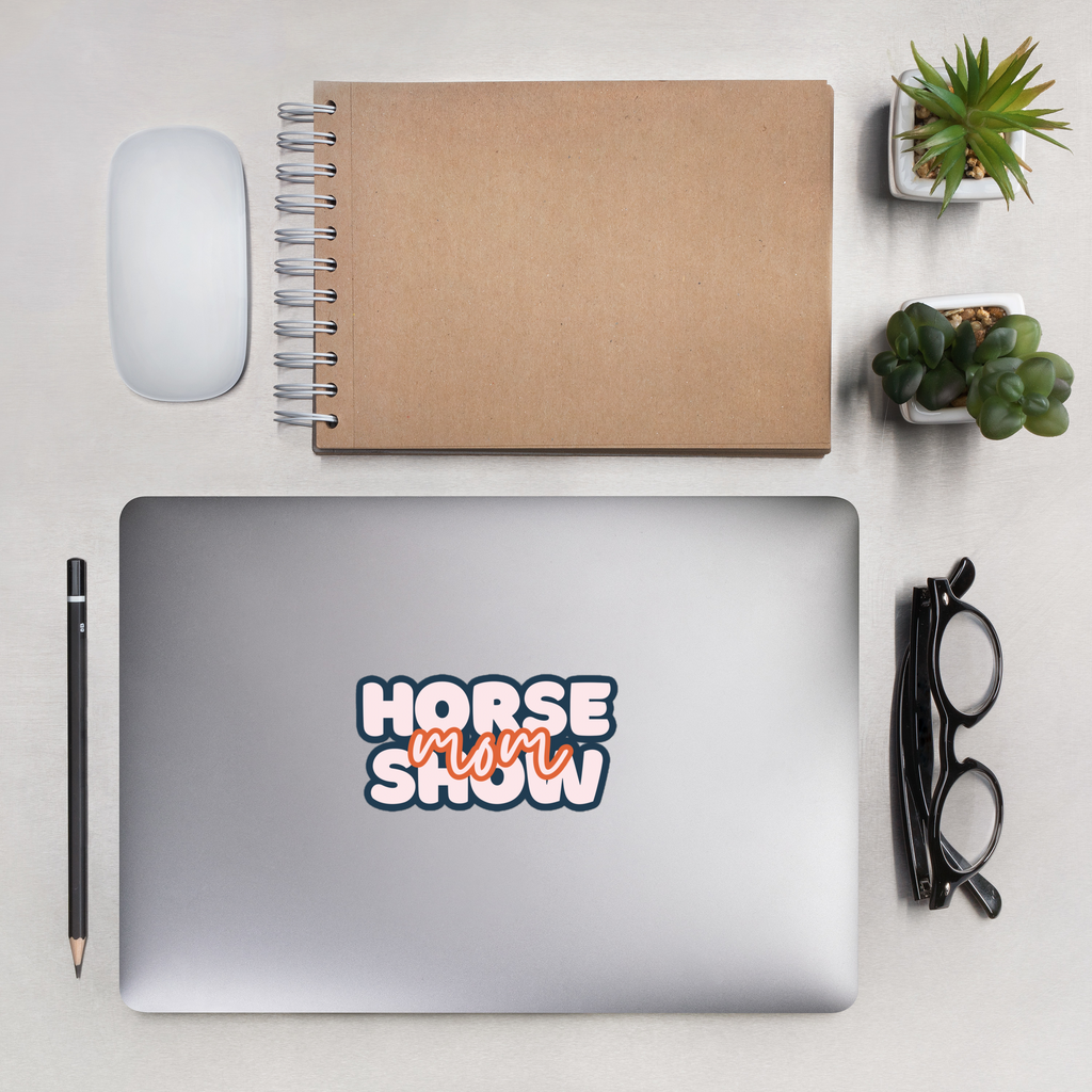 Laptop with 'Horse Mom Show' sticker on a desk with notebook, mouse, and plants.