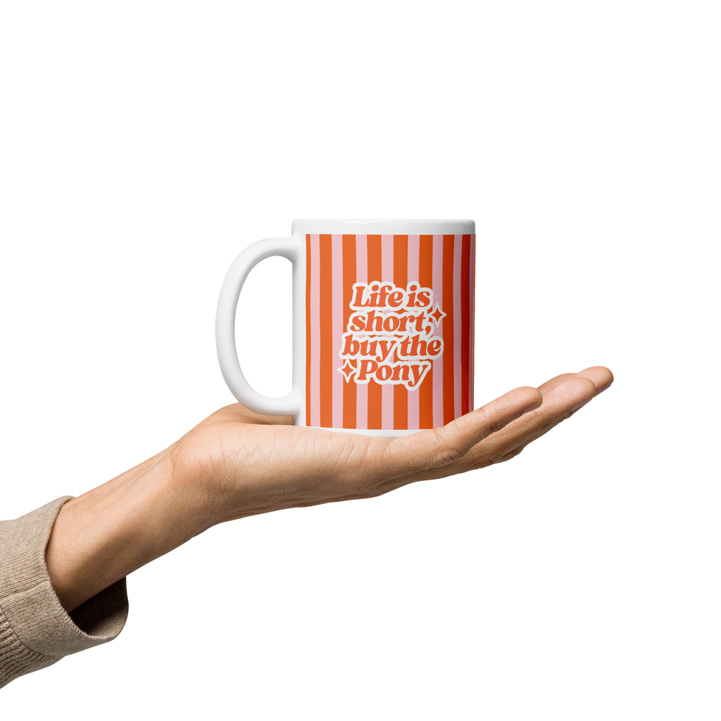 A hand holding a white ceramic mug with orange vertical stripes and the text 'Life is short, buy the pony' in orange and white lettering.